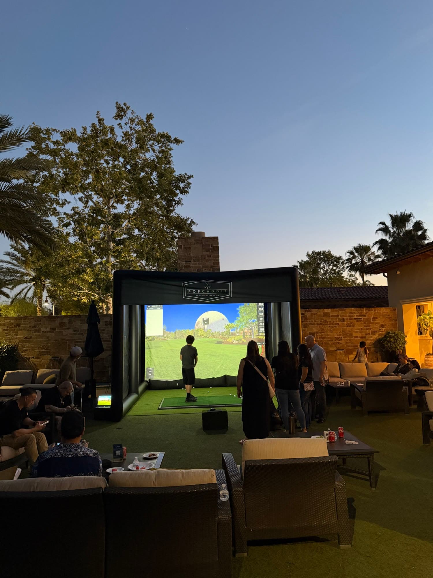 Guests playing the golf simulator on a terrace at dusk (PopCaddie event)